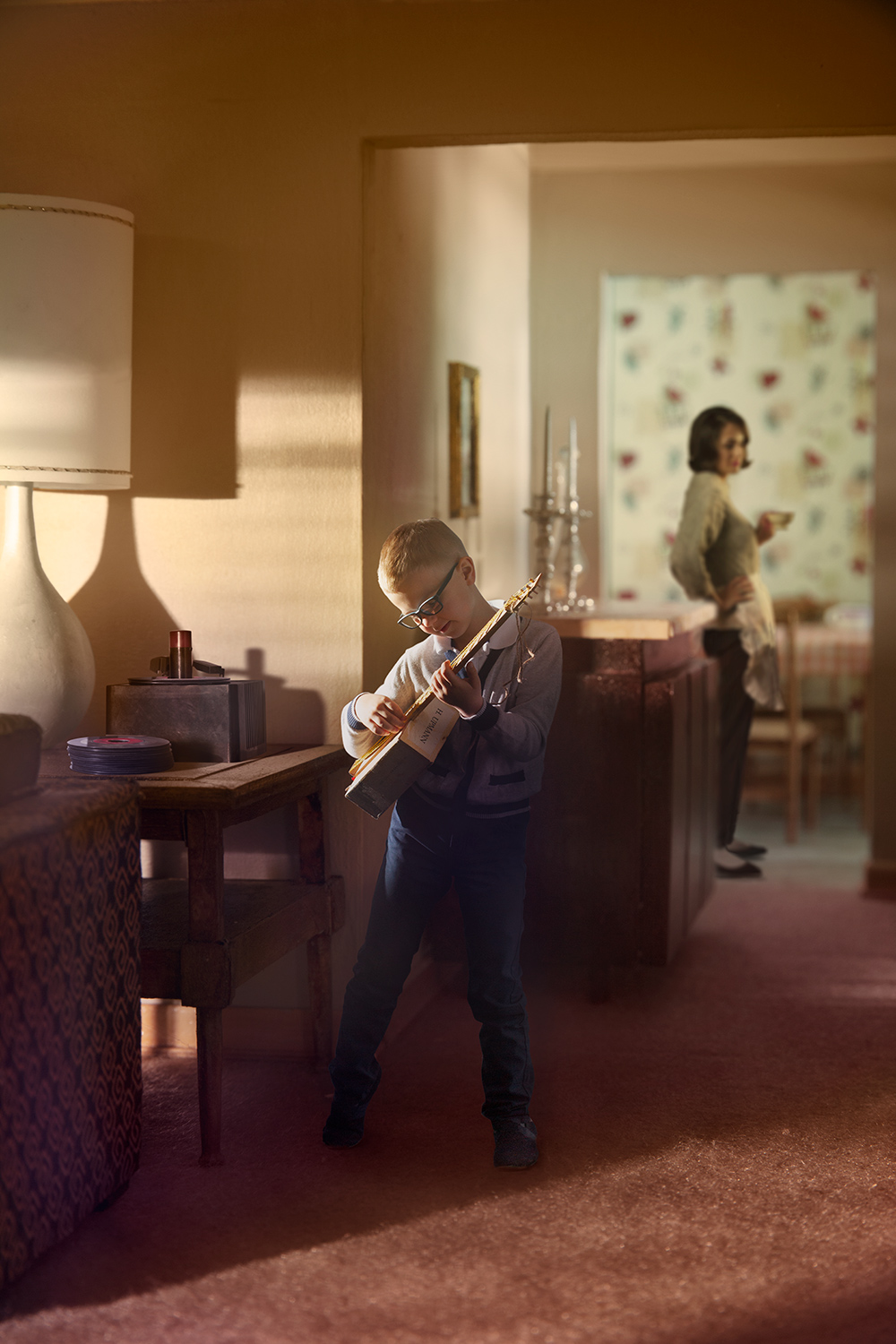Boy enthusiastically playing toy guitar in 1960s sunlit suburban living room miniature dollhouse set