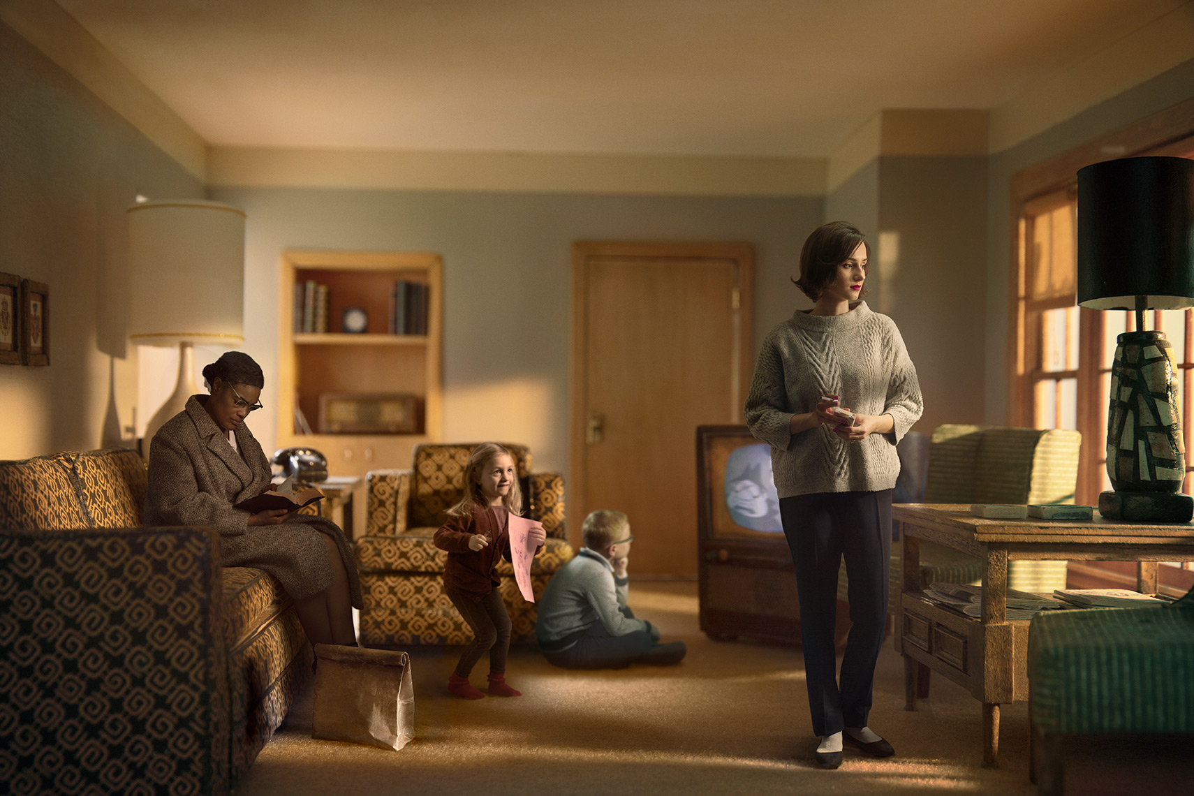 Late afternoon 960s suburban living room: African-American housekeeper sits on the couch, boy watches TV, girl approaches mother lost in thought who gazes out the picture window