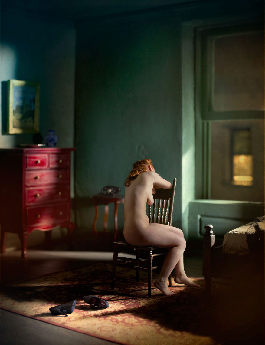 A photomontage homage to Edward Hopper, set in a 1940s’ New York apartment at night, a s eated nude, red-haired young woman seen from behind, bathed in light from a street lamp outside, gazing out the window, high heels lay on the floor next to her.