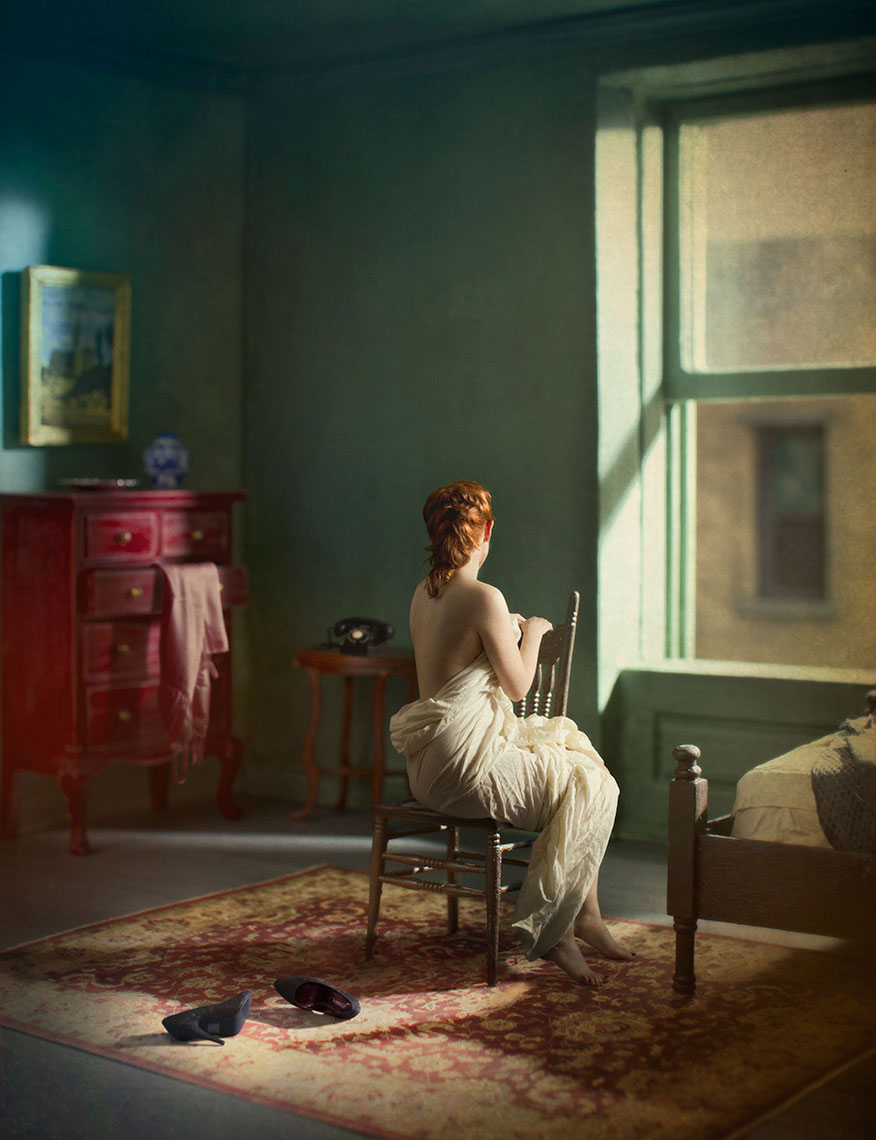 A photomontage homage to Edward Hopper, set in a 1940s’ New York apartment at night, a seated nude, red-haired young woman seen from behind, bathed in light from a street lamp outside, gazing out the window, high heels lay on the floor next to her.