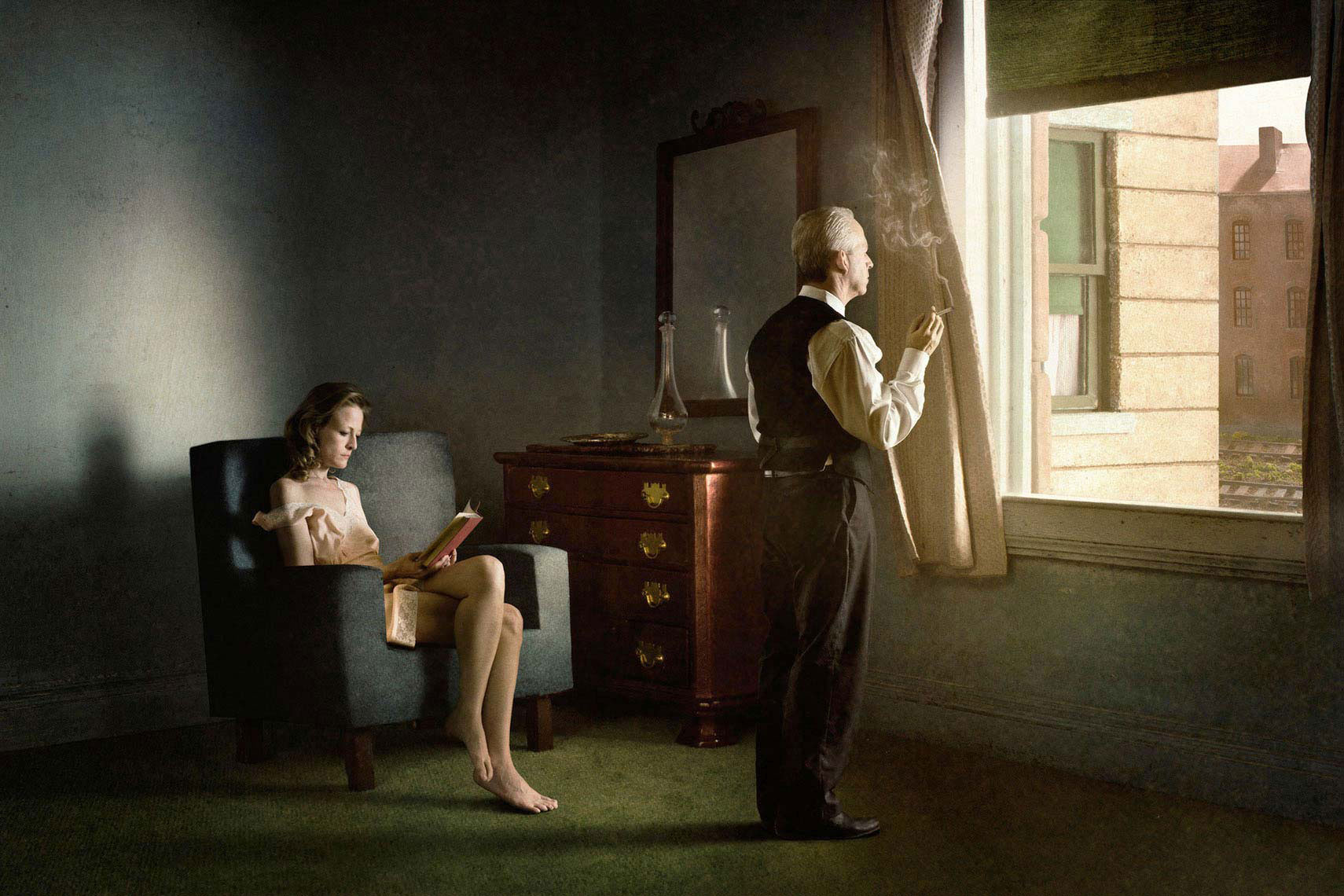 A photomontage homage to Edward Hopper’s painting, “Hotel by a Railroad”, set in a 1940s’ hotel room, a dishwater-blonde woman wearing a pale pink slip sits in an armchair reading, while her male companion, stands smoking a cigarette and gazing in contemplation out the window onto the railroad tracks.