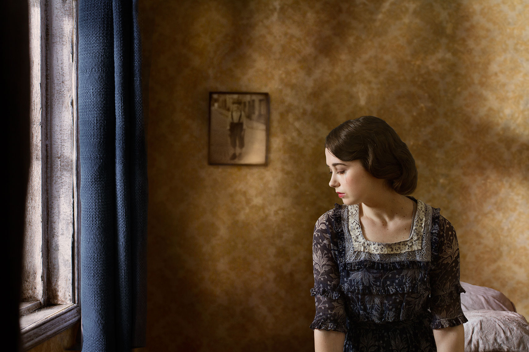 Painterly photomontage of 1930s beautiful young dark-haired mother sitting by the bedroom window, a tear rolling down her cheek, a picture of a young boy on the wall behind her.