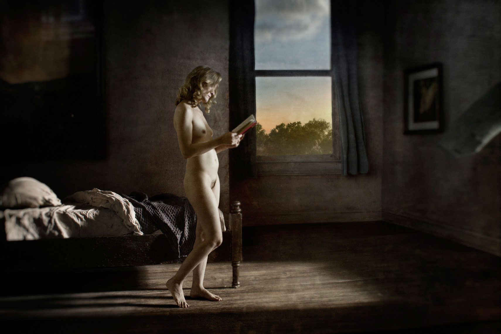 A photomontage homage to Edward Hopper, set in a 1940s’ bedroom, a nude, dishwater-blonde woman stands in a rectangle of bright sunlight, reading a book, an unmade bed in the background.
