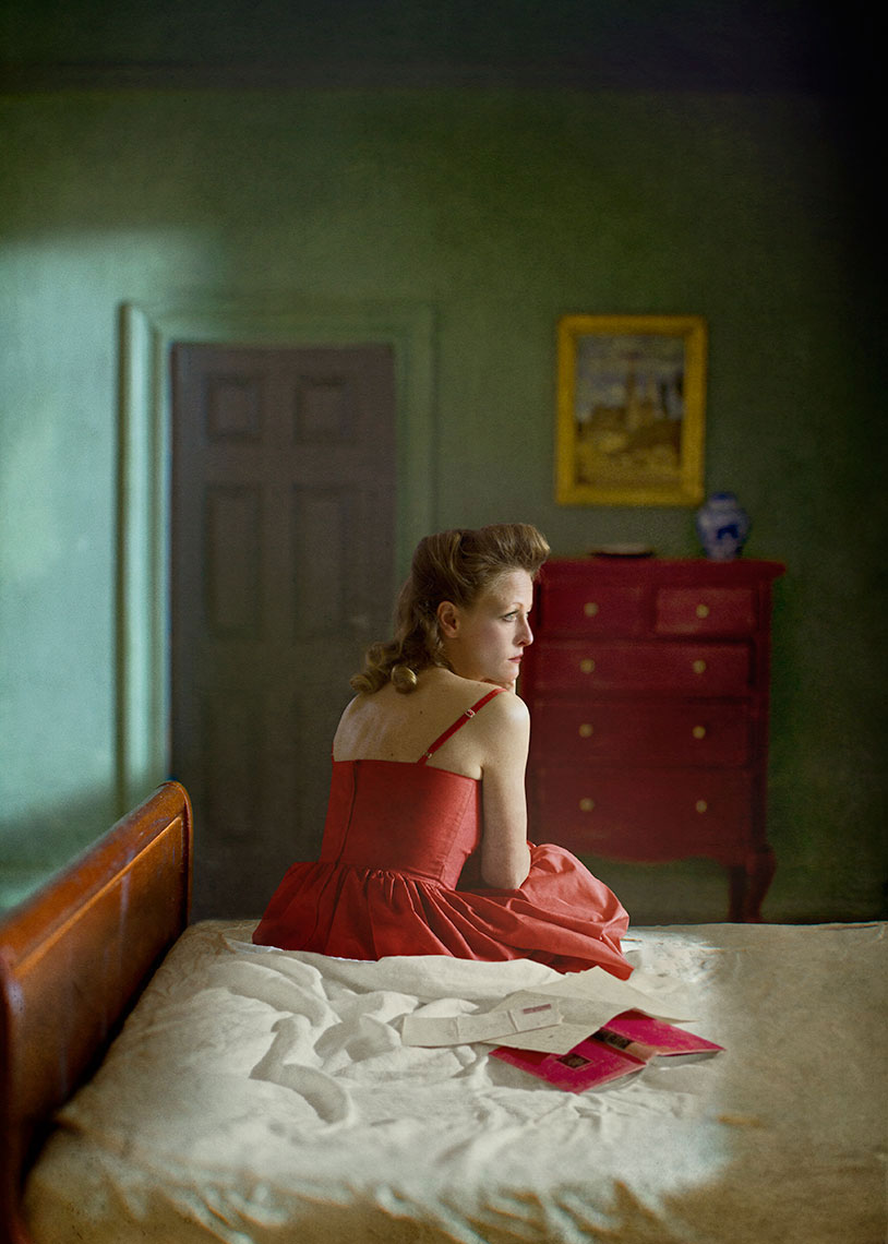 A photomontage homage to Edward Hopper, set in a 1940s’ New York apartment,  a dishwater-blonde woman in a spaghetti strap red dress, sits on the edge of an unmade bed, an open book and letter splayed on the rumpled sheets next to her.